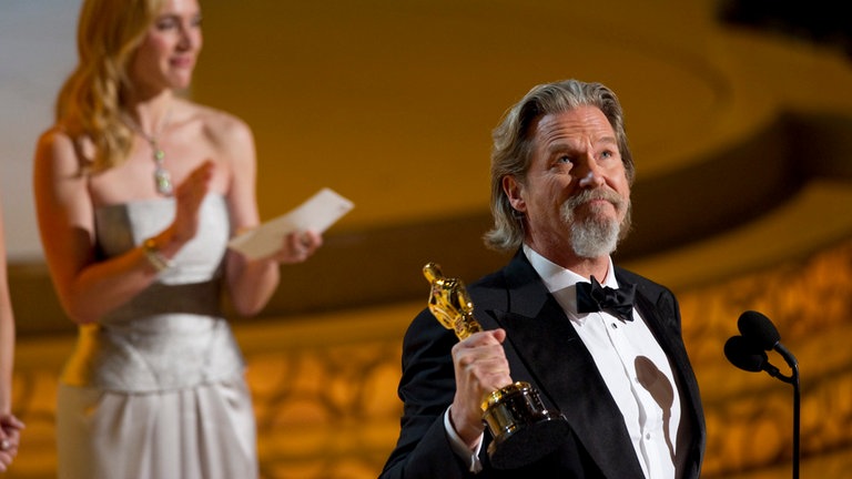 Der Schauspieler hält seine Oscar-Trophäe hoch, die er für seine Rolle in „Crazy Heart“ gewonnen hat. Im Hintergrund ist die britische Schauspielerin Kate Winslet zu sehen. 