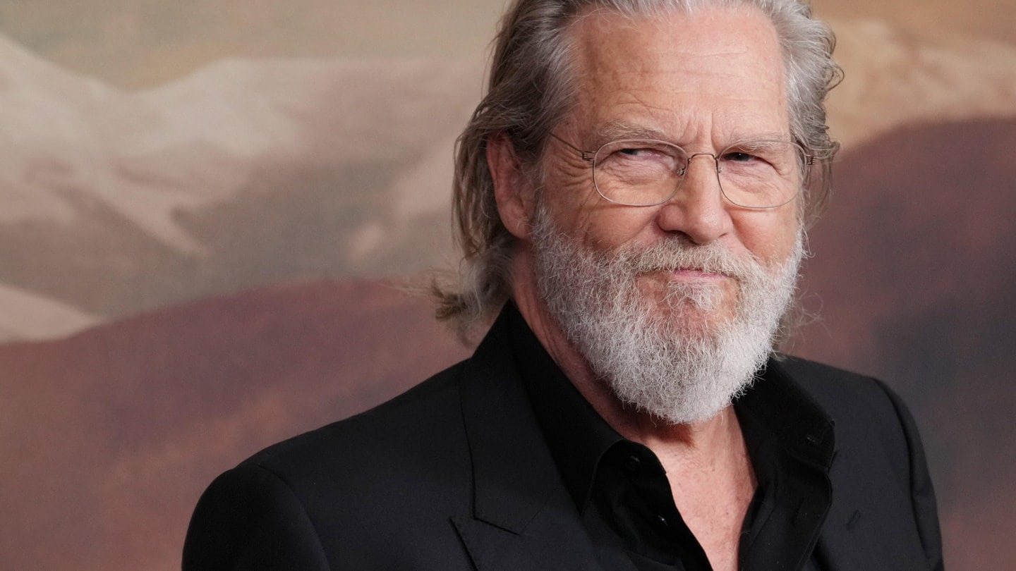 Jeff Bridges trägt sein graues Haar lang und eine randlose Brille. Er lächelt auf einer Premierenfeier.