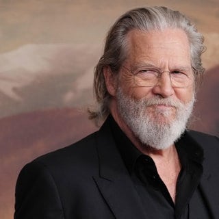 Jeff Bridges trägt sein graues Haar lang und eine randlose Brille. Er lächelt auf einer Premierenfeier. 