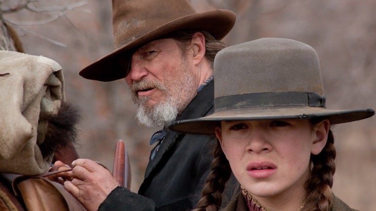 Jeff Bridges als Cowboy mit Augenklappe steht hinter der Schauspielerin Hailee Steinfeld, die einen Hut trägt.