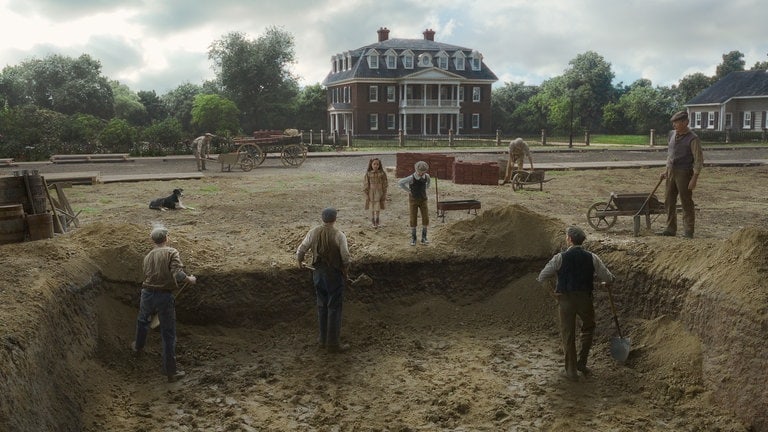 Einstellung aus dem Film „Here“: Menschen stehen an einer großen Baugrube. Hier soll ein Haus entstehen, das den Schauplatz des Films darstellt.