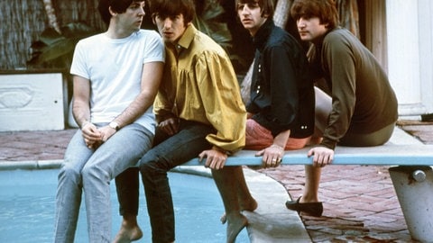 Paul McCartney, George Harrison, Ringo Starr und John Lennon sitzen auf einem Sprungbrett am Pool. 