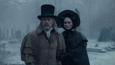 Schauspieler Willem Dafoe (links) und Lily-Rose Depp (rechts) stehen auf einem verschneiten Friedhof im Film „Nosferatu“ (2024)