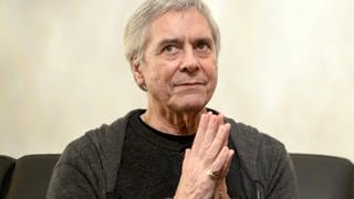 Choreograf John Neumeier, ein älterer Mann mit Falten im Gesicht und grauem Haar, dunkel gekleidet, sitzt am Donnerstag, 29. Jänner 2015, während eines Interviews mit der Austria Presse Agentur (APA) in Wien vor einer beigen Wand. Er faltet die Hände vor der Brust, an seinem rechten kleinen Finger trägt er einen goldenen Ring.