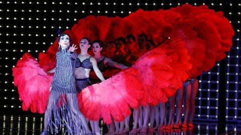 Ruth Brauer-Kvam spielt im Musical "Chicago", hinter ihr Tänzerinnen in Dessous mit roten Burlesque-Federfächern