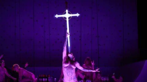 Eine nackte Frau auf der Bühne schluckt scheinbar ein großes Kreuz - Szene aus Florentina Holzingers Opernperformance "Sancta"