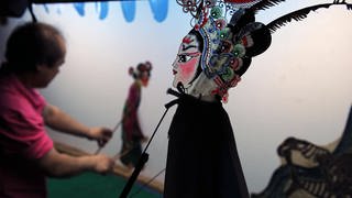 Schattentheaterspieler einer chinesischen Theatertruppe beim Spielen. Im Vorodergrund eine traditionelle chinesische Frauen-Schattenfigur.