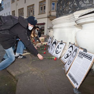 Mehrere Personen legen an  den Portraits der Ermordeten von Hanau rote Nelken nieder. 