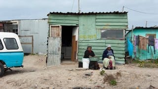 Zwei Frauen sitzen vor einer Wellblechhütte im einem Armenviertel bei Kapstadt, Südafrika