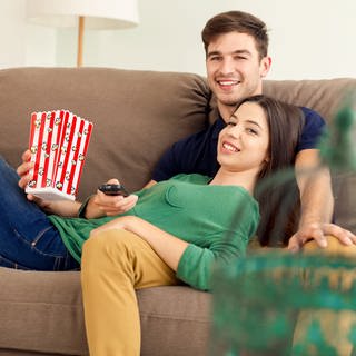 Ein Paar sieht gemeinsam auf der Couch Fernsehen und isst Popcorn