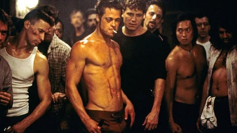 Eine Gruppe Männer steht in einem schlecht beleuchteten Raum im Kreis, in ihrer Mitte Brad Pitt, jung, mit freiem Oberkörper, er blutet am muskulösen bacuh. Er hat eine Zigarette im Mund und ein angeschwollenes Auge.