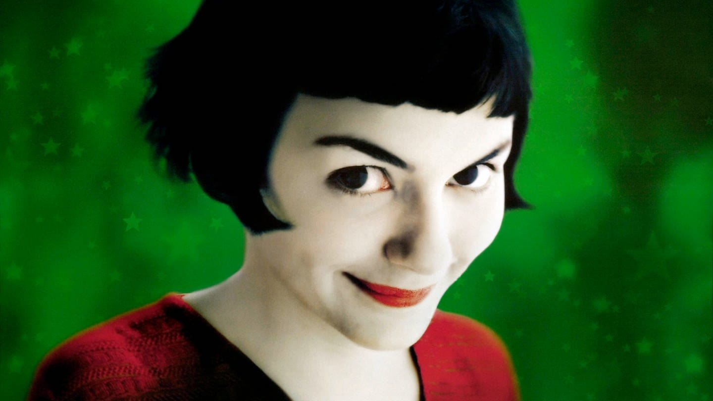 Audrey Tautou als Amelie Poulain im roten Kleid vor grünem Hintergrund, schaut in die Kamera
