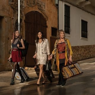 Drei Frauen laufen mit Koffern eine Straße entlang (Filmstill zur Serie "Land of Women" auf Apple TV+)