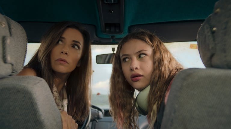 Zwei Frauen schauen über die Schulter in Richtung Kamera (Eva Longoria und Victoria Bazúa, Filmstill zur Serie "Land of Women" auf Apple TV+)
