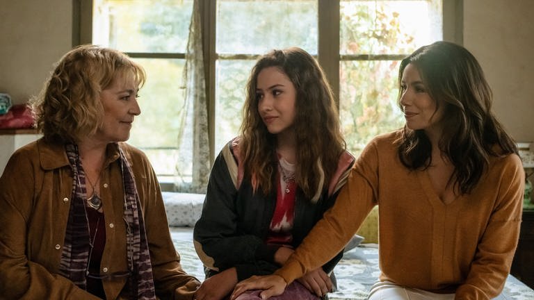 Drei Frauen aus drei unterschiedlichen Generationen sitzen beisammen und schauen sich lächend an (Bilder zur Serie "Land of Women" auf Apple TV+)
