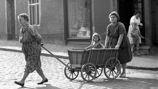 Frauen aus drei Generationen gehen mit einem Handwagen spazieren (1960).