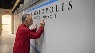 Francis Ford Coppola schreibt etwas an die Wand, auf der Megalopolis steht