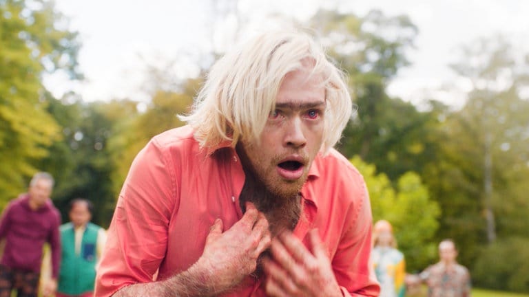 Filmstill: Ein Mann mit blonden Haaren scheint zu ersticken. Seine Augen sind rot angelaufen. 