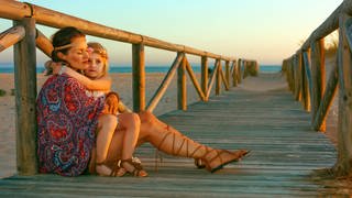 Als Hippie gekleidete Mutter hält Tochter im Arm, am Strand