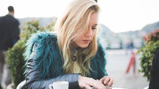 Junge Frau in Lederjacke, sitzt in einem Cafe und benutzt ein Tablet