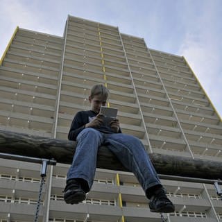 Junge spielt mit seinem Nintendo vor einem Hochhaus