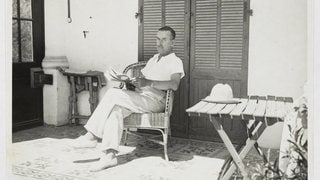 Thomas Mann sitzend mit einem Buch in der Hand auf der Veranda