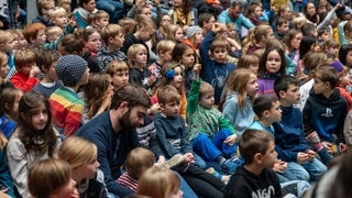 viele Kinder sitzen auf dem Boden und warten auf das Live-Hörspiel