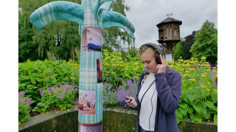 Autorin Kseniya Fuchs steht mit Kopfhörer auf neben einer Palme 