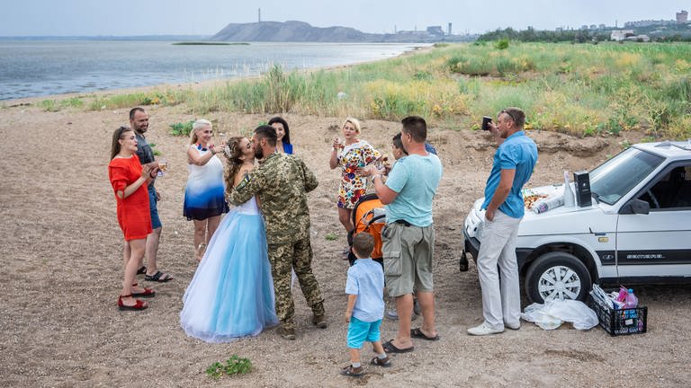 Eine Frau im Brautkleid und ein Mann in Uniform, feiern ihre Hochzeit am Strand in der Nähe des Azovstal-Werks, der ukrainischen Stadt Mariupol.