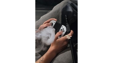 Eine Shisha rauchende Person mit Spielkonsole in der Hand