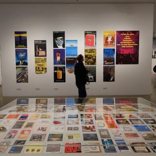Eine Person schaut sich Plakate mit politischem Inhalt in einer Ausstellung des Künstlers Klaus Staeck an