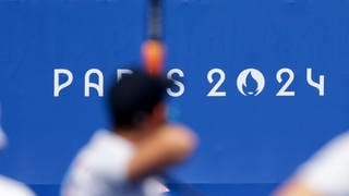 Bogenschießer vor dem Logo der Olympischen Spiele in Paris 2024