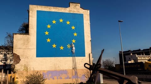 Ein Banksy-Mural: Man sieht einen Bauarbeiter, der aus einer Europaflagge einen Stern herausmeißelt