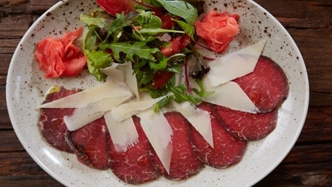 Teller mit Carpaccio vom Rind mit Parmesanhobeln und Rucola.