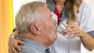Eine Altenpflegerin hilft einem älteren Mann beim Trinken