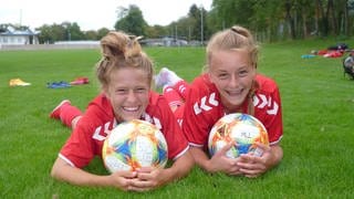 zwei junge Fußballspielerinnen liegen im Gras und lachen in die Kamera