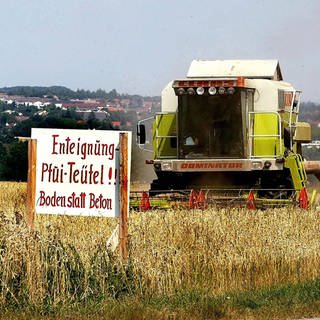 Mähdrescher bei der Ernte hinter einem Schild mit dem Schriftzug - Enteignung - Pfui Teufel! Boden statt Beton -  in Leinfelden-Echterdingen