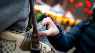 Taschendiebstahl: Eine Hand zieht Geldscheine aus einer Handtasche