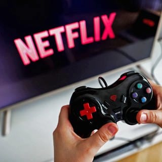 Netflix will sich in Zukunft verstärkt um den Ausbau seiner Gaming-Abteilung kümmern - Hände halten den Controller einer Spielekonsole vor einem TV-Bildschirm auf dem das Netflix-Logo angezeigt wird.