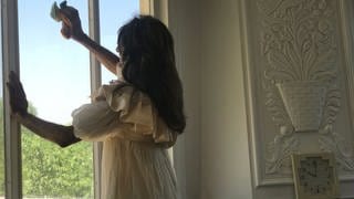Hamideh im weißen Kleid beim Fensterputzen 