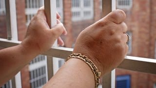 Zwei Hände halten die Gitter vor einem Gefängnisfenster