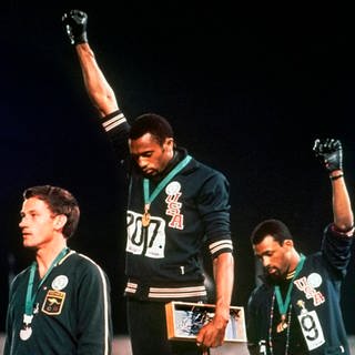 Der australische Silbermedaillengewinner Peter Norman (links), die Amerikaner Tommie Smith (Mitte) und John Carlos ihre behandschuhten Fäuste zu einem Menschenrechtsprotest erheben.