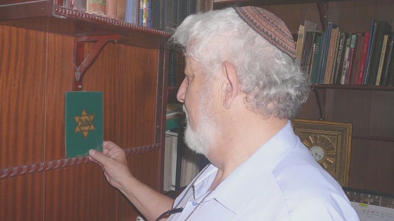 Links vom Arbeitstisch hängt der gelbe Judenstern auf grünem Grund. Den fand Moshe Rosenfeld vor 40 Jahren in der Wohnung eines Shoah-Überlebenden, der ihm seine Bibliothek verkaufte. Der Judenstern öffnet ein Fenster in Moshes Familiengeschichte. 