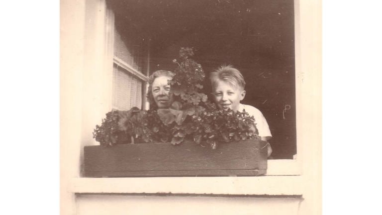 Mit seiner Mutter Ludwina Ims lehnt Alfons am Fenster. Die Familie wohnt 1953 nach dem Auszug aus dem Kalkofen 1960 in der Barackensiedlung Engelshof. Alfons Ludwig Ims: „Die Familie meines Vaters war ein Sozialfall, aber die Nazis haben aus dem Sozialfall Asozialität gemacht.“ Und noch in den 1960er Jahren galten die Leute hier als „sozial krank“. „Wenn es eine Heldin gibt, dann war das meine Mutter. Sie hat darum gekämpft, rauszukommen. Und ohne sie hätte ich das nicht geschafft.“