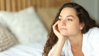 Pensive woman on a bed looking away, Pensive serious woman lying on a bed looking away in the bedroom, Pensive serious woman lying on a bed looking away in the bedroom model released, Symbolfoto , 14.11.2022