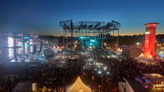 Abendstimmung auf dem Techno-Festival "Nature One" mit bunten Lichtern, feierndem Publikum und Bühnen und Zelten