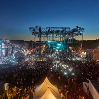 Abendstimmung auf dem Techno-Festival "Nature One" mit bunten Lichtern, feierndem Publikum und Bühnen und Zelten