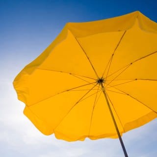 A yellow sunshade against a deep blue sky. Symbolfoto