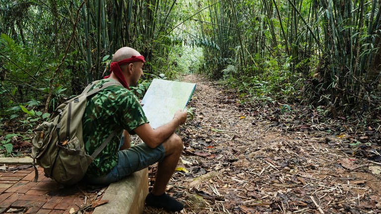 Travelling man sitting and looking at the map in the bamboo forest