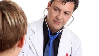 A sick young patient is being examined by a medical practitioner who is using a stethoscope.